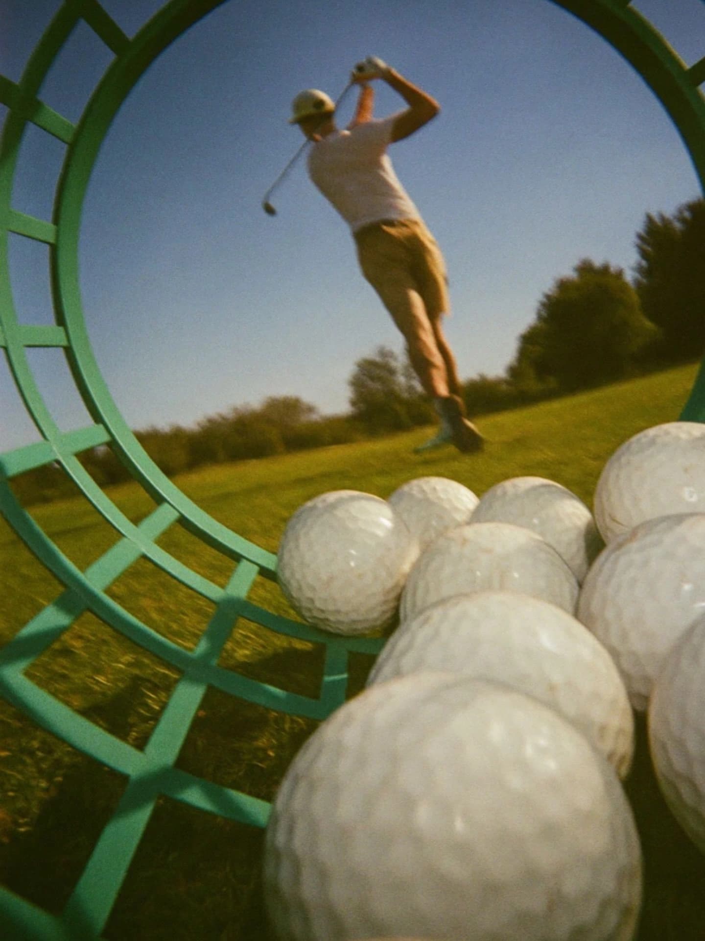 A golfer finishing a swing, seen through a basket of range balls